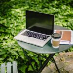 From above of modern laptop placed on round table near documents and cup of takeaway coffee in green park