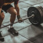 A focused weightlifter prepares to lift a heavy barbell in an indoor gym setting.